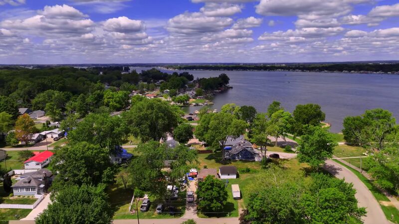 The Image Shows a Scenic View of Lake Arlington, with A Lush, Tree-Lined Residential Area Near the Water, Dotted with Homes and Greenery, Under a Sky Filled with Puffy White Clouds