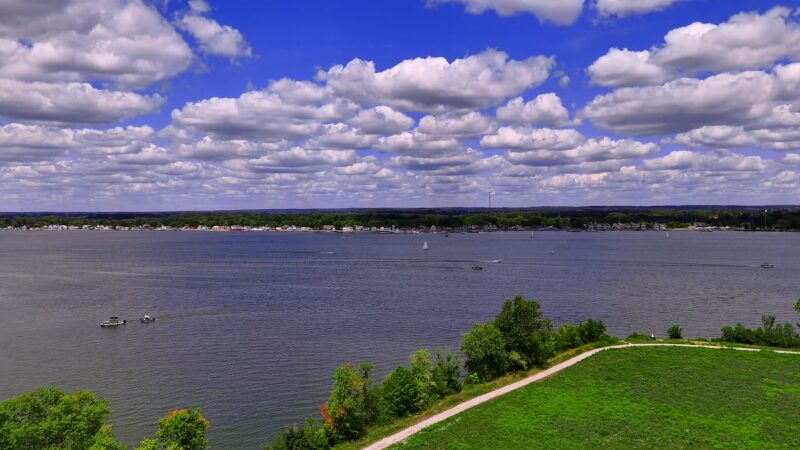 The Image Shows a Wide View of Lake Arlington with Boats Scattered Across the Water, Surrounded by Lush Greenery and A Bright Blue Sky Filled with Fluffy Clouds, Creating a Serene and Inviting Atmosphere