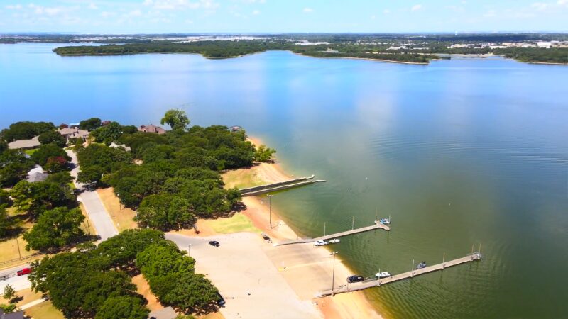 The Image Shows a Calm, Expansive View of Lake Arlington with A Boat Ramp and Dock, Surrounded by A Tree-Covered Residential Area and Clear Skies, Providing a Peaceful Lakeside Setting