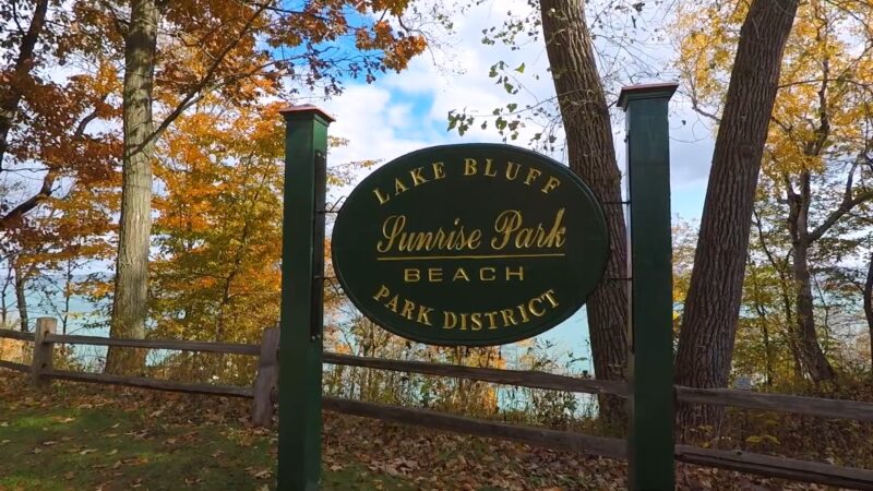 sign at Sunrise Park Beach in Lake Bluff, Illinois, surrounded by colorful autumn foliage and trees, with the serene lake visible in the background