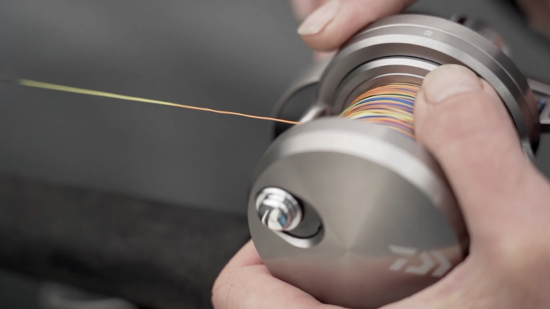 A Person Spooling Multi-Colored Braided Fishing Line onto A Reel