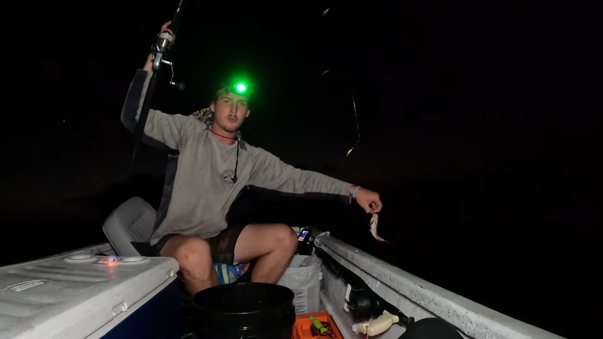 A man wearing a headlamp fishing at night from a small boat